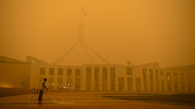 A man cleans the forecourt of Parliament House surrounded by smoke haze in Canberra. Picture: AAP