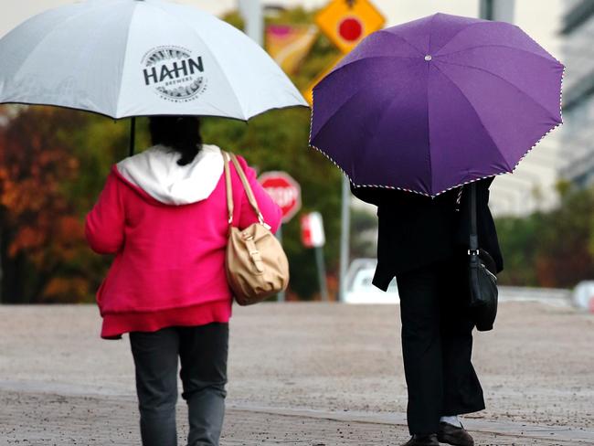 People holding umbrellas dodge the rain at Sydney Olympic Park. Picture Toby Zerna