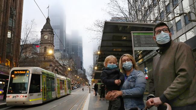 A family don masks as they wait for a tram on Collins street. Picture: David Crosling