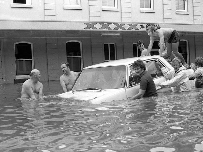 Mates give a hand to try to move a car trapped by flood waters in Margaret S, Brisbane. Picture by Geoff McLachlan
