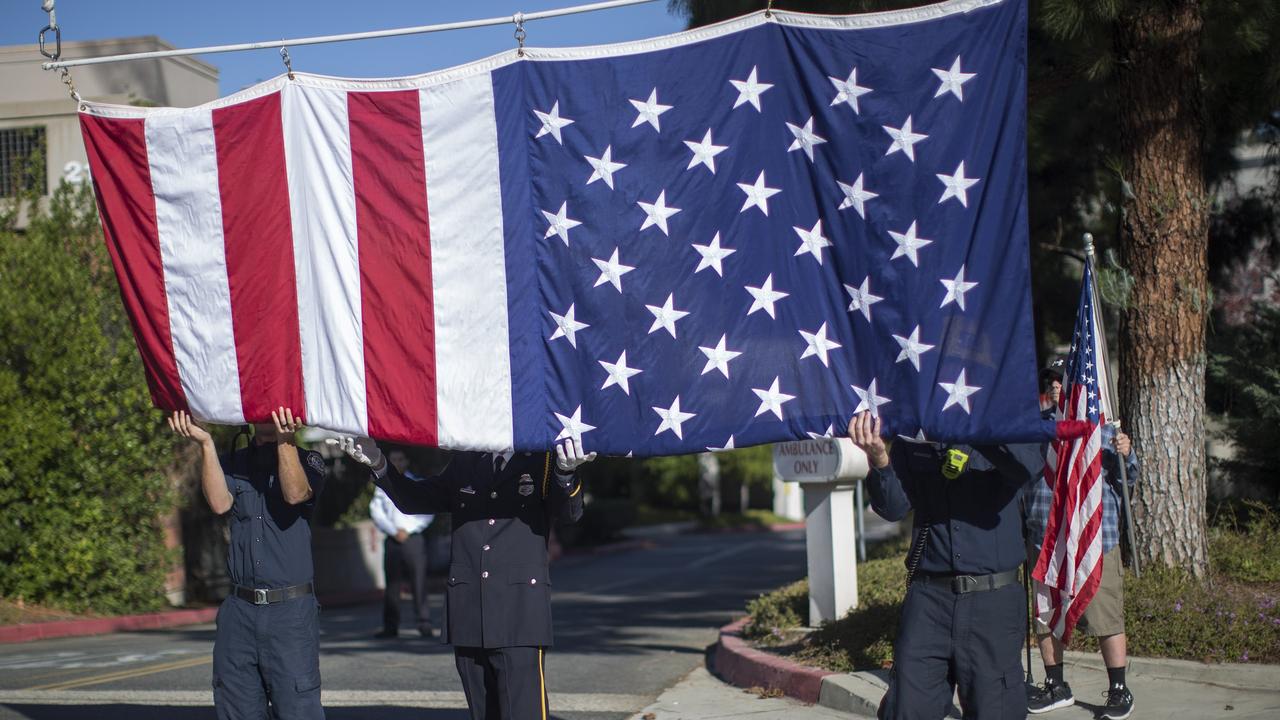 Firefighters raise a flag at Los Robles Hospital to hang over the procession carrying the body of Ventura County Sheriff Sgt. Ron Helus, who was killed in the mass shooting. Picture: AP