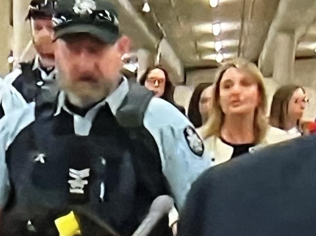 Optus CEO  Kelly Bayer Rosmarin ( in cream) being escorted by AFP at Parliament House in Canberra. Picture: Sky News