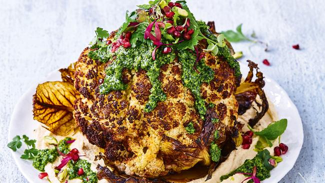 A whole roasted cauliflower with hummus and green herb dressing.