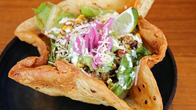 The Taco Bowl filled with coriander and lime rice, black beans, corn salsa, guacamole, lettuce, crema, cheese, chipotle honey vinaigrette, served in a deep-fried tortilla bowl.