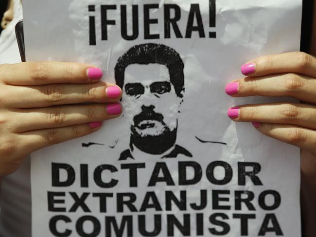 An anti-government protester holds a sign with a photo of President Nicolas Maduro and a message that reads in Spanish: Out! Dictator, Foreigner, Communist during a women’s march against repression in Caracas on Saturday. Picture: Ariana Cubillos/AP