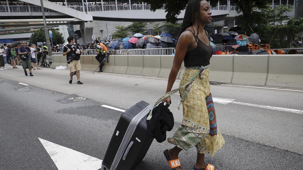 A foreigner with her luggage walks on a road as protesters gather. Picture: Vincent Yu/AP