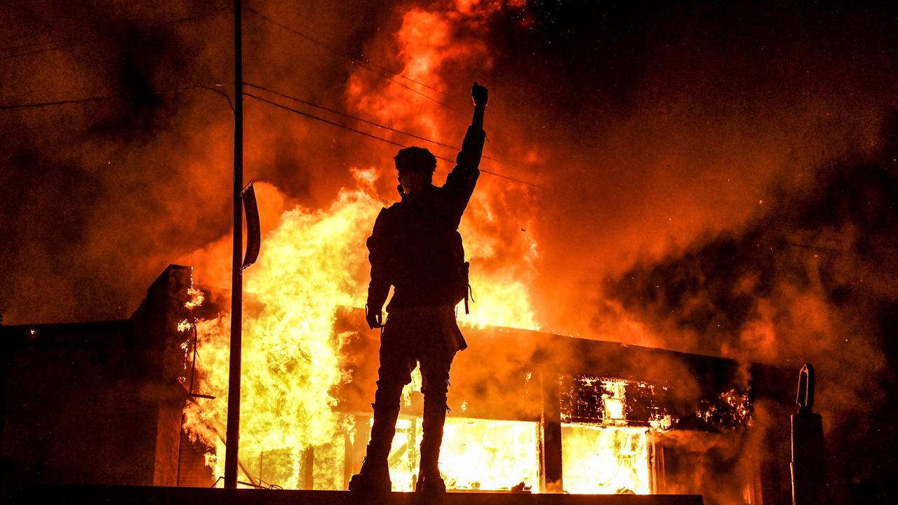 A protester throws their fist in the air in front of a burning building in Minneapolis. Picture: Chandan Khanna / AFP