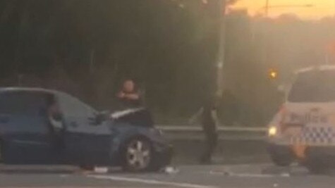 A Gold Coast police officer draws his gun on a machete-wielding motorist after he crashed his car on an M1 overpass.