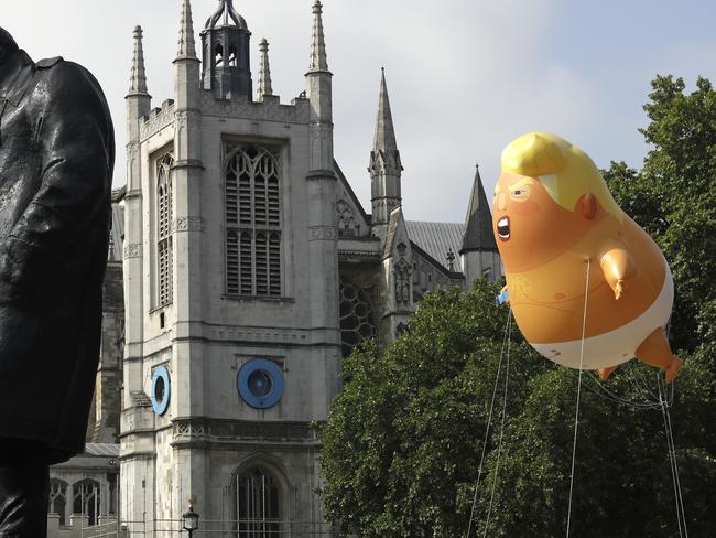 A six-meter high cartoon baby blimp of U.S. President Donald Trump hovers next to the statue of former British Prime Minister Winston Churchill, as it is flown as a protest against his visit, in Parliament Square in London, England, Friday, July 13, 2018. (AP Photo/Matt Dunham)
