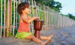 Piccola bambina felice suona musica etnica sul tradizionale tamburo a mano africano djembe, godendosi il tramonto sulla spiaggia oceanica. Bambini stile di vita sano. Viaggio, attività di famiglia su isola tropicale vacanze estive.