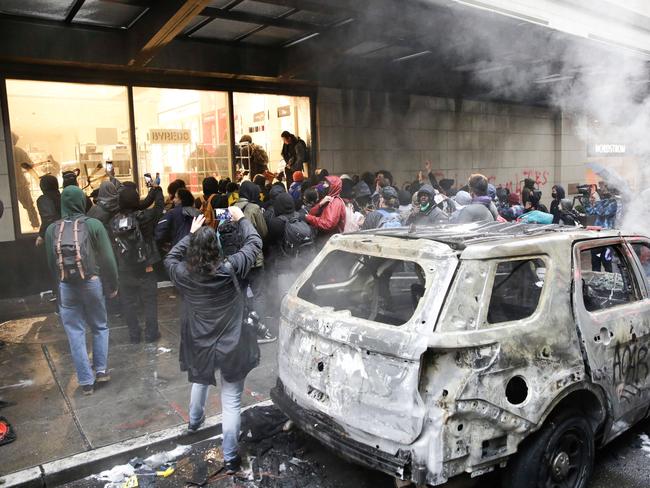 People loot a Nordstrom store near a burned police car following demonstrations protesting the death of George Floyd. Picture: Jason Redmond