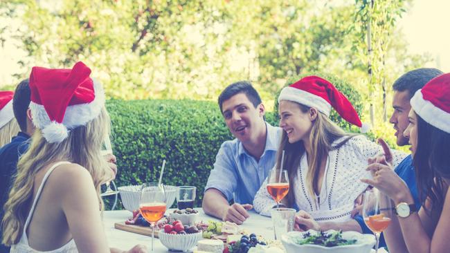 Group of people celebrating with Santa hats. They are having fun at a Summer Christmas party, and there is food on the table. There are also cocktails. Istock