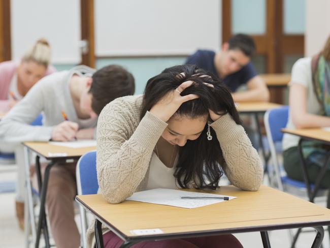 Stressed student sitting in a classroom at a table while doing an exam- STOCK PIC