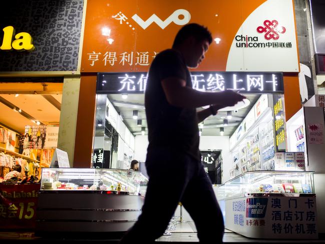 A pedestrian holding a mobile phone walks past signage for China Unicom Ltd. at a store in the Gongbei district of Zhuhai, Guangdong province, China, on Saturday, Nov. 15, 2014. Investors piled into Shanghai shares on the first day of exchange-link trading, buying the maximum amount allowed in a sign of global demand for mainland equities as China opens up its $4.2 trillion market. Photographer: Brent Lewin/Bloomberg