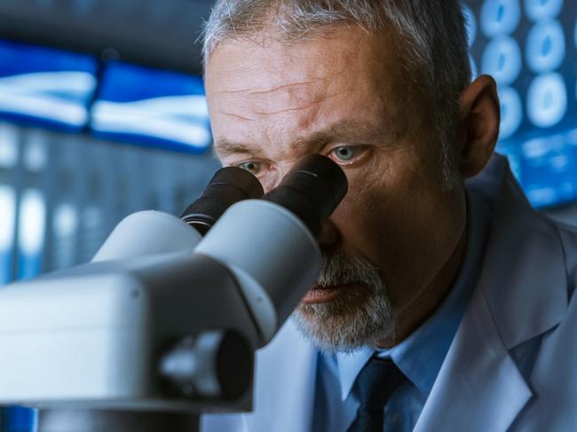 Senior Medical Research Scientist Looking under the Microscope in the Laboratory. Neurologist Solving Puzzles of the Mind and Brain. In the Laboratory with Multiple Screens Showing MRI / CT Brain Scan Images.