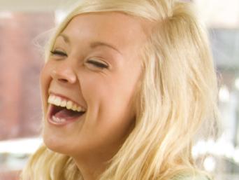 Young couple laugh together while standing in their new home littered with cardboard moving boxes.