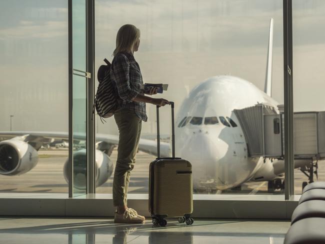 Woman with boarding passes and hand baggage looks out the terminal window on a large airlinerStart of the journey.