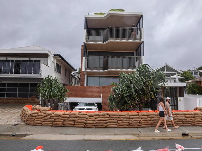 People walk past a block of units surrounded by sand bags to protect it from the storm surge of large waves generated by Tropical Cyclone Alfred at Currumbin on the Gold Coast on March 6, 2025. The outer fringe of Tropical Cyclone Alfred started whipping eastern Australia on March 6, bringing drenching rains and record-breaking waves to a heavily populated region rarely hit by typhoons. (Photo by David GRAY / AFP)