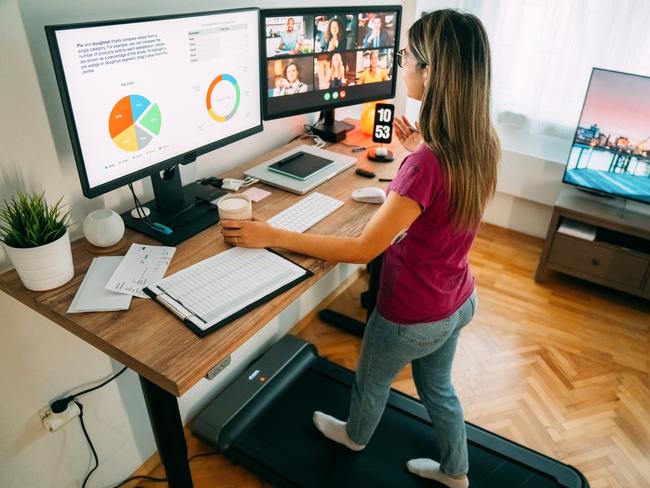 Woman working from home at standing desk is walking on under desk treadmill