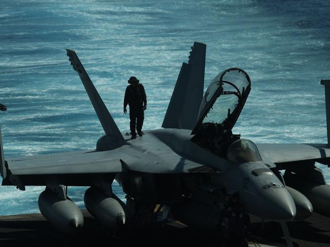 A sailor inspects atop an FA-18 hornet fighter jet during a routine training aboard US aircraft carrier Theodore Roosevelt in the South China sea which is transiting after participating in operations in Syria, Iraq and Afghanistan. Picture: AFP PHOTO / TED ALJIBE