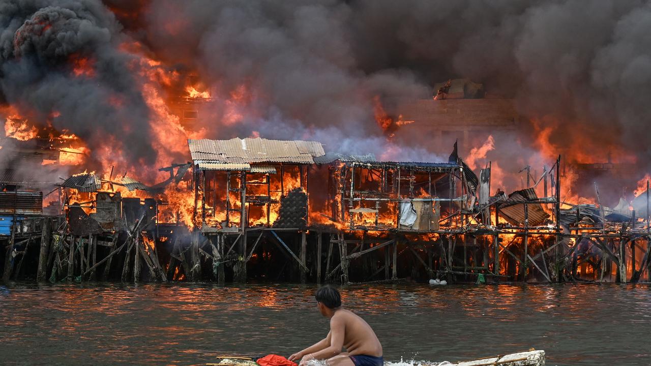 A man watches houses on fire at Tondo in Manila on November 24, 2024. Raging orange flames and thick black smoke billowed into the sky, as fire ripped through hundreds of houses in a closely built slum area of the Philippine capital Manila. (Photo by JAM STA ROSA / AFP)