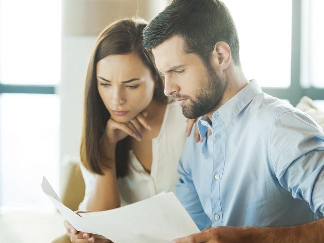 Concentrated young man holding documents and looking at them while woman sitting close to him and holding hand on chin