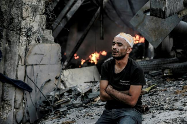 An injured man sits in front of a smouldering building in the aftermath of an Israeli strike on Gaza City on Thursday