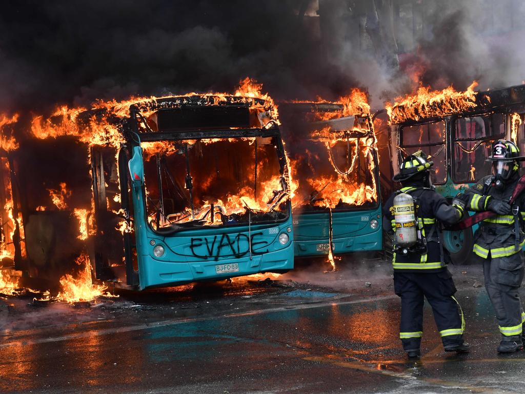 Chilean firefighters extinguish burning buses during clashes between protesters and the riot police in Santiago. Picture: AFP