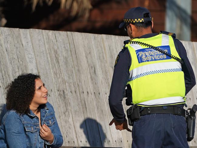 Victoria Police Protective Services Officers speak to a woman at St Kilda beach in Melbourne, Monday, April 13, 2020. Victoria Police issued 433 fines between 11:00pm on Thursday and 11:00pm on Easter Sunday after conducting thousands of spot checks across the state. A shutdown of non-essential services is in effect Australia wide in a bid to slow the spread of the coronavirus (COVID-19) disease.(AAP Image/Scott Barbour) NO ARCHIVING