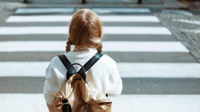 Seen from behind trendy pupil in white sweatshirt with backpack crossing crosswalk and going to school outdoors in the city.