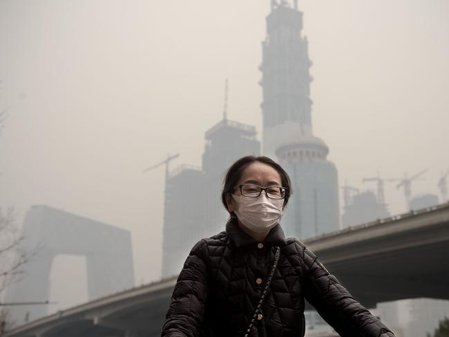 A woman wearing a protective pollution mask rides a bicycle in Beijing on March 20, 2017.   The last large coal-fired power plant in Beijing has suspended operations, with the city's electricity now generated by natural gas, the state news agency reported as smog enveloped the Chinese capital this weekend. / AFP PHOTO / NICOLAS ASFOURI