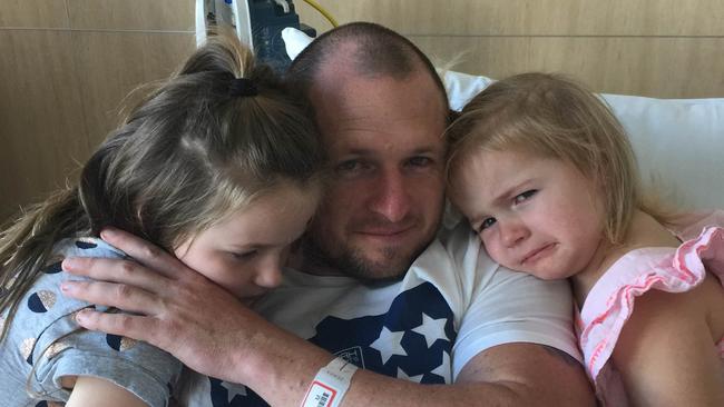 Shane Randall in hospital with his daughters after being injured in a boat crash on the Broadwater.