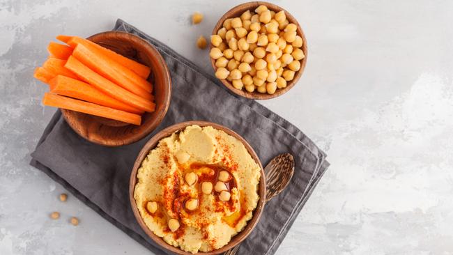 Hummus, fresh carrot sticks and boiled chickpeas in wooden bowls.