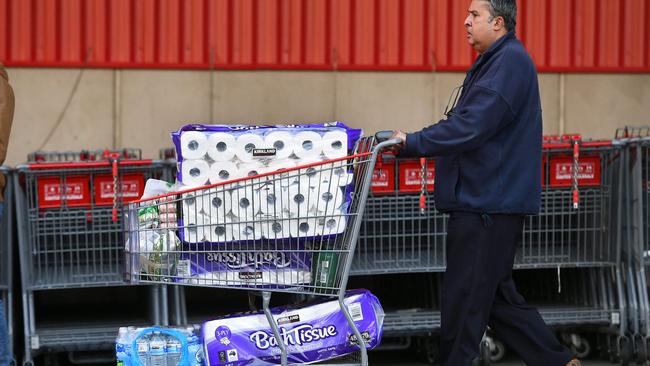 A man leaves Costco in Melbourne yesterday with a trolley full of toilet paper and water. Photo: William West / AFP