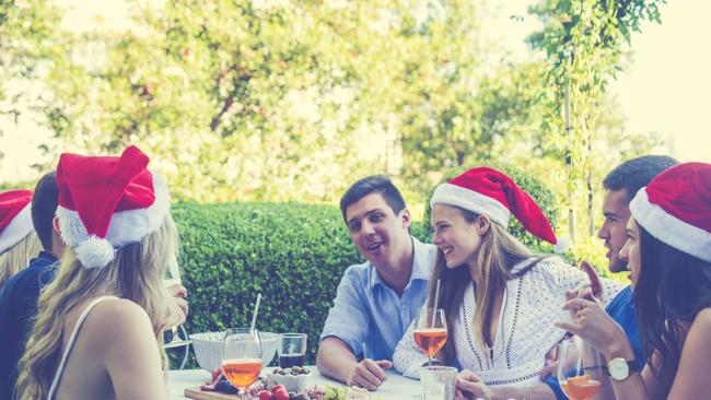 Group of people celebrating with Santa hats. They are having fun at a Summer Christmas party, and there is food on the table. There are also cocktails. Istock