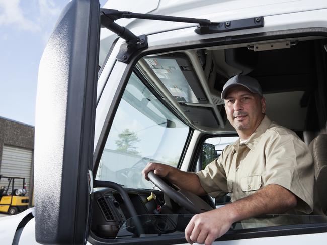 Truck driver (30s) sitting in cab of semi-truck.