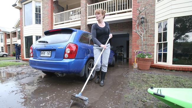 Chris Mackinnon sweeps away water and mud from her home at Old Noarlunga. Picture: STEPHEN L