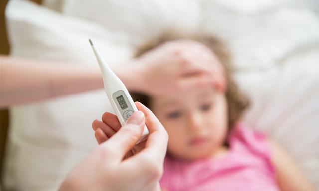 Close-up thermometer. Mother measuring temperature of her ill kid. Sick child with high fever laying in bed and mother holding thermometer. Hand on forehead.