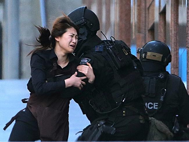 A hostage runs to armed tactical response police officers for safety after she escaped from a cafe under siege at Martin Place. Picture: AP Photo/Rob Griffith