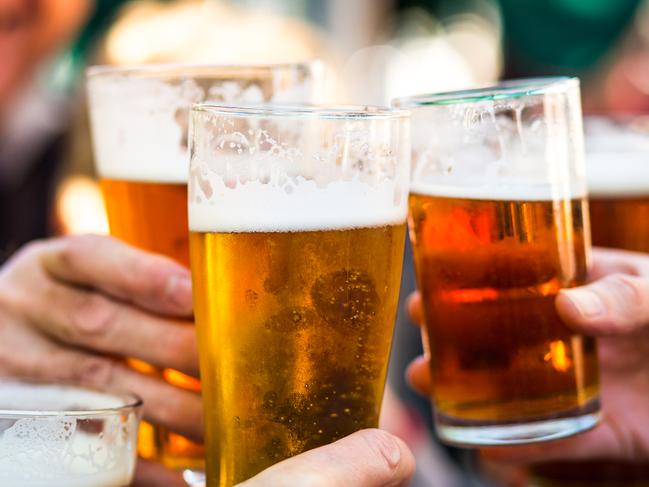 Close up color image depicting a group of people celebrating with a toast. The people cheers their glasses of beer (pints of beer) together in a gesture of celebration, togetherness and happiness. The people are defocused in the background, while focus is on the glasses of beer in the foreground. Room for copy space.