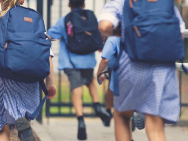 School children running away. They are wearing uniforms and carrying backpacks. They are having a race. Multi ethnic group with Asian, Caucasian and Aboriginal children. Rear view