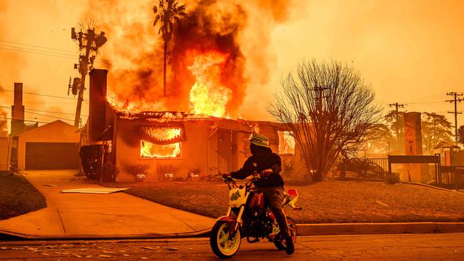 A motorcyclist stops to watch a burning home during the Eaton fire in the Altadena area. Picture: AFP