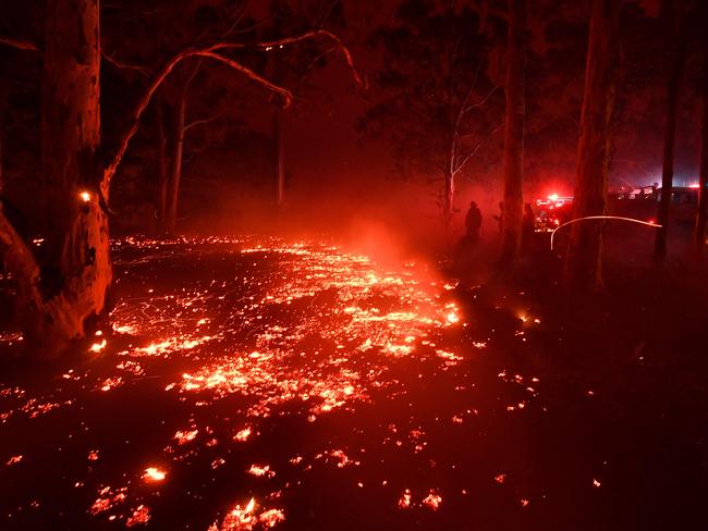 Burning embers cover the ground as firefighters (back R) battle against bushfires around the town of Nowra in the Australian state of New South Wales on December 31, 2019. - Thousands of holidaymakers and locals were forced to flee to beaches in fire-ravaged southeast Australia on December 31, as blazes ripped through popular tourist areas leaving no escape by land. Picture: Saeed Khan/AFP