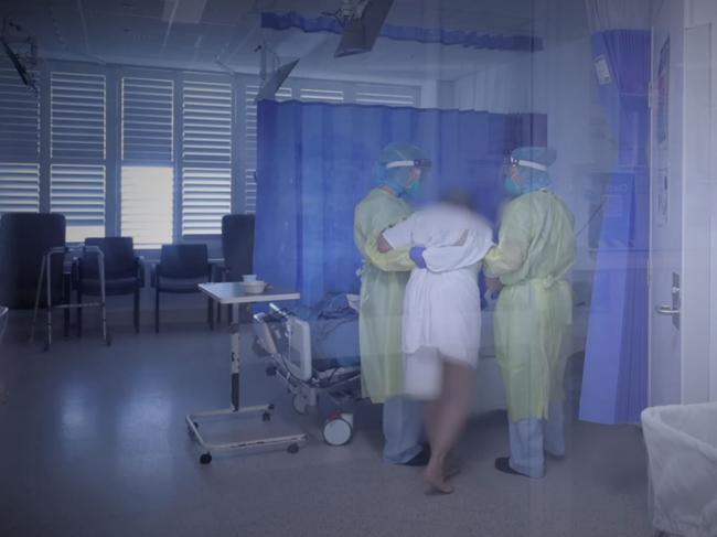 A patient struggling to stand is helped to their bed.