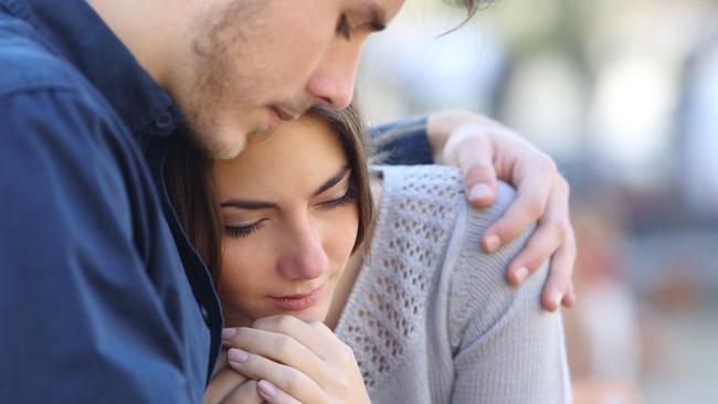 Man comforting his sad mourning friend embracing her in a park