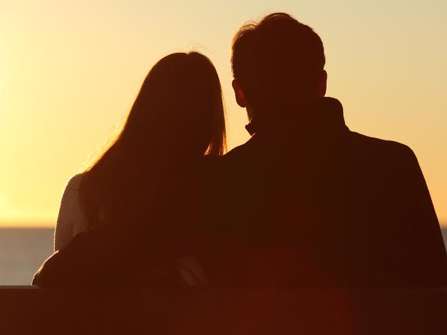 Back view of a couple silhouette hugging and watching sun on the beach