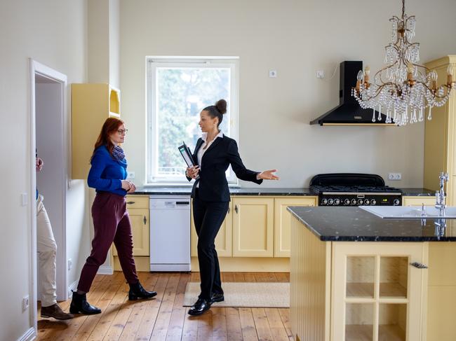 Female realtor gesturing to customers at empty new apartment. Couple is entering kitchen. Saleswoman is showing home to man and woman.