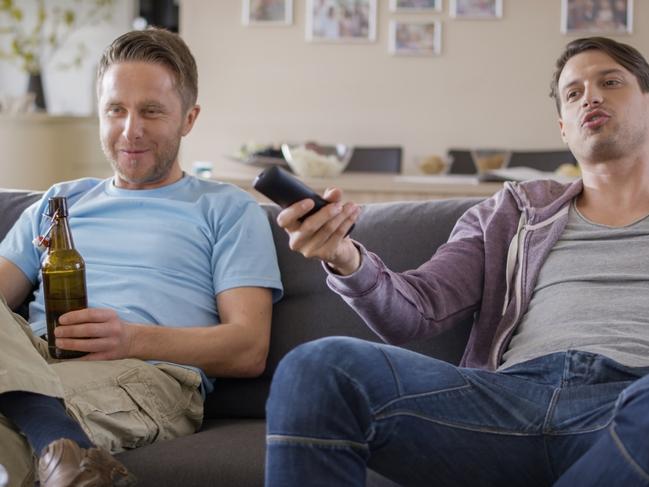 Young men sitting on sofa and enjoying drink while watching TV at home.