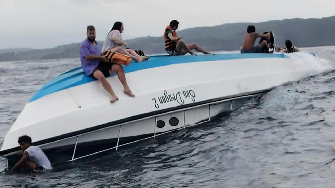 Survivors sit on the hull of the capsized boat in Nusa Penida, Bali. Picture: AFP Photo / Klungkung District Police