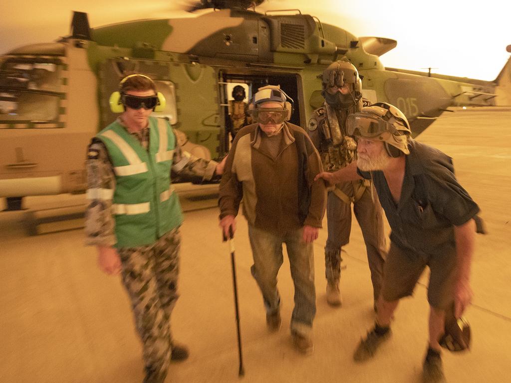 Mr Frank Delaney and Mr Warren Usher of Yalwal, NSW is assisted from an 808 Squadron MRH90 Military Support Helicopter after being evacuated from his remote rural property to the east of the Moreton National Park and in the direct fire front of the Tianjara Fire burning north through ten thousand hectares of national park and bushland. Picture: ADF